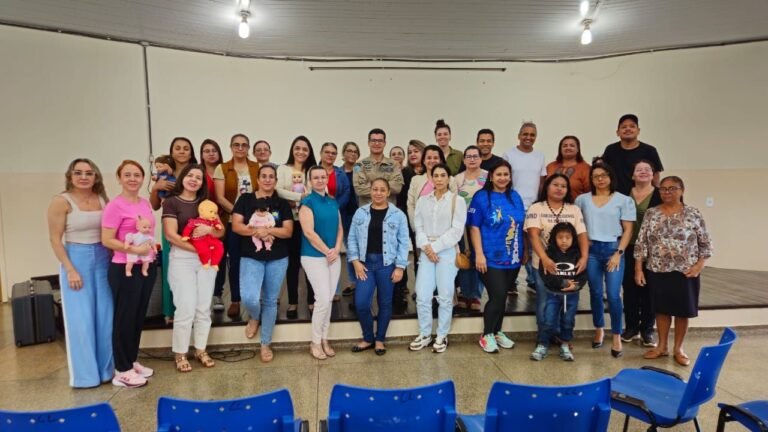 Diverse group of adults and children posing on a small stage in a hall for a group photo.