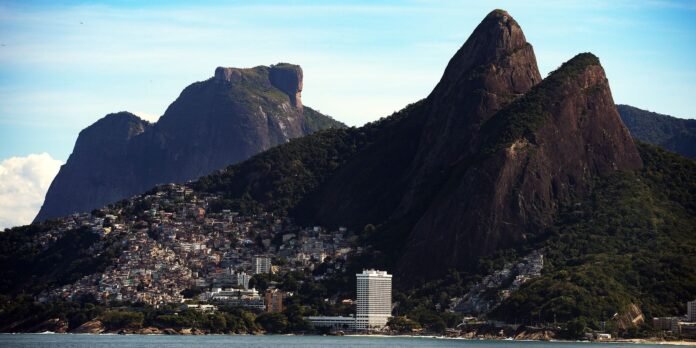 Coastal city built along a bay with steep forested mountains and a tall white hotel by the shore behind the urban area.