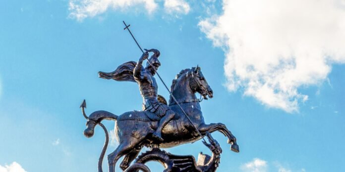 Bronze statue of a mounted warrior brandishing a spear against a bright blue sky.