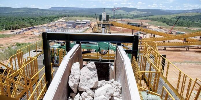 Industrial quarry scene with large rock dump in a concrete chute and yellow safety rails, conveying machinery in the background.