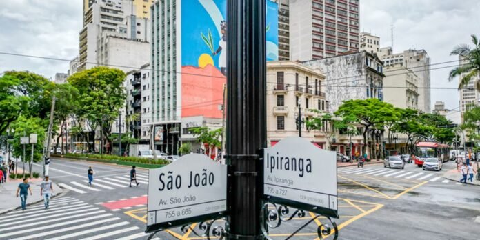 Signage for São João and Ipiranga avenues at a busy city intersection with crosswalks and pedestrians.