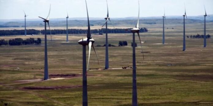 Row of wind turbines across a flat grassy landscape under a clear sky, forming a wind farm.