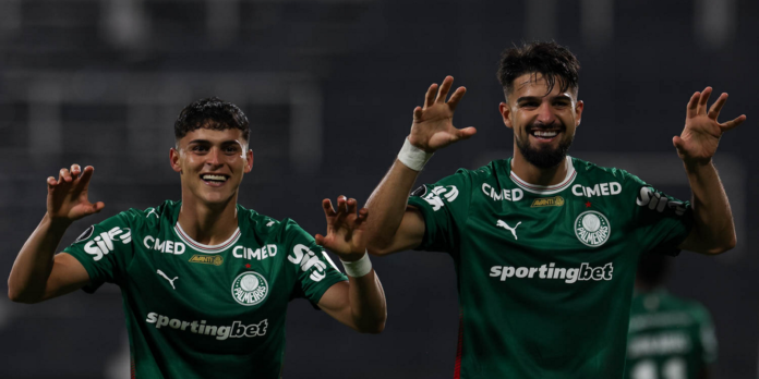 Two Palmeiras players in green jerseys celebrate, hands raised and smiling on the field.