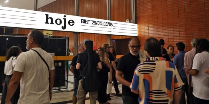 Group of people talking in a modern lobby with wood panel walls and a bold white sign reading 'hoje'.