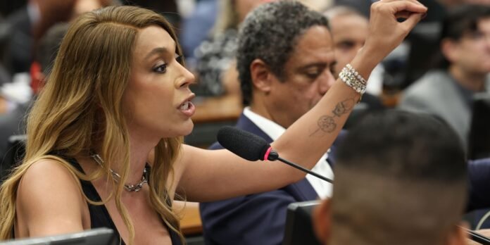 Woman testifying at a hearing, speaking into a microphone with her arm raised to emphasize her point.