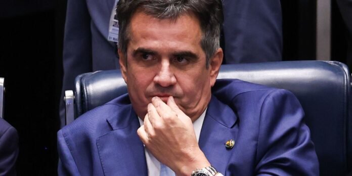 Man in a blue suit sits in a leather chair, chin resting on his hand, looking thoughtful during a formal meeting.