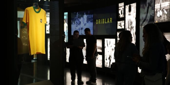 Yellow Brazilian soccer jersey on display in a dim museum gallery with visitors nearby.