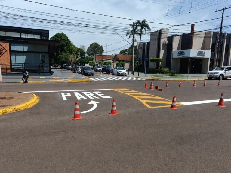 Street intersection with crosswalk, the word 'PARE' painted on the road, and orange traffic cones guiding traffic closing lanes nearby.