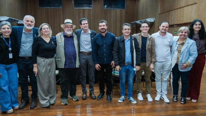 Twelve adults standing in a row in a wood-paneled room, posing for a group photo.