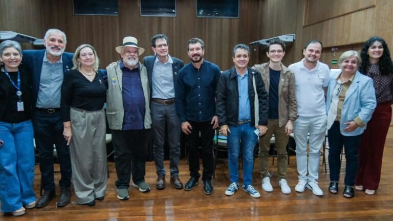 Twelve adults standing in a row in a wood-paneled room, posing for a group photo.