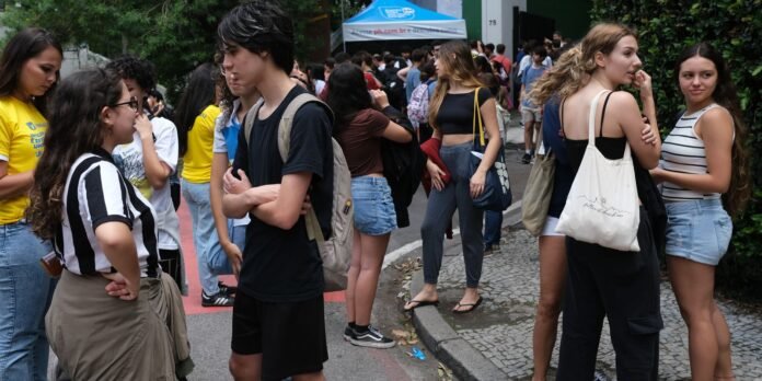 Group of students standing and talking on a street at an outdoor campus event, tents in the background near a doorway.