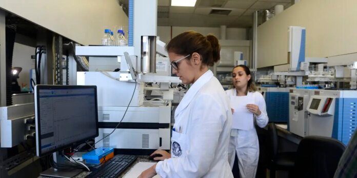 Two scientists in white coats work in a modern lab with a computer and large analytical instrument.