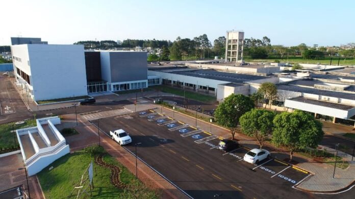 Aerial view of a modern campus with white buildings, a paved parking lot, and green landscaped areas seen from above.