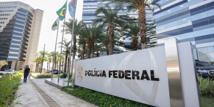 Exterior view of a Polícia Federal building with a large sign, palm trees, flagpoles, and a modern glass facade in a sunny urban plaza.