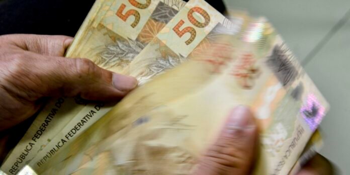 Close-up of hands counting a stack of Brazilian 50-real banknotes.