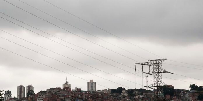 Dense urban hillside with a large transmission tower and power lines under gray, overcast skies.