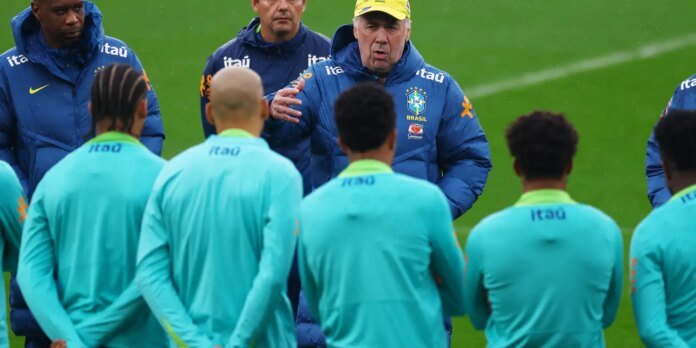 Brazil national team coach Tite speaks to players during training, gesturing with his hand on a green field.