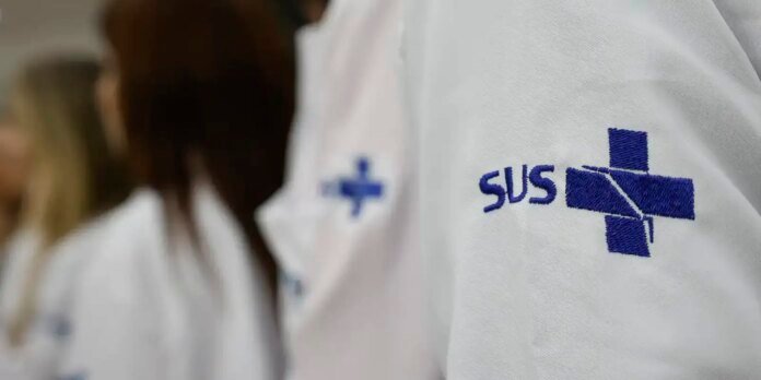Close-up of a white medical coat with a blue cross emblem and 'SUS' embroidered on it.