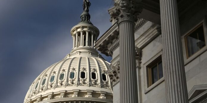 Close-up view of a white neoclassical dome with ornate windows and a statue-topped cupola, beside tall fluted columns.