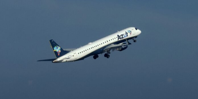 Azur Airlines Airbus A320 climbs after takeoff, white fuselage, blue underbelly, colorful map-design tail against a clear sky.