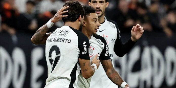 Two soccer players in white and black kits hug in celebration on the field during a match.