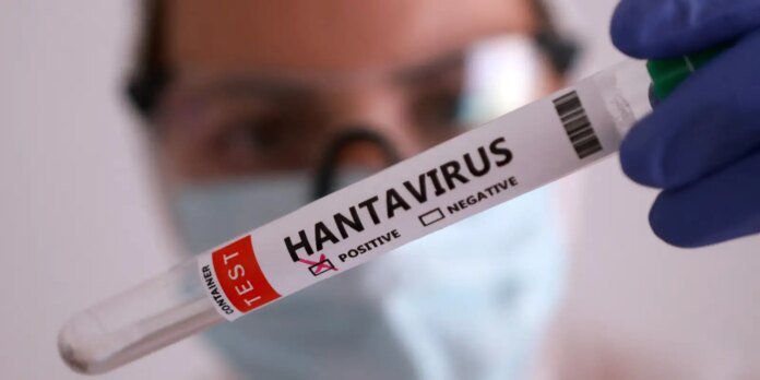 Lab worker in a mask and blue gloves holds a test tube labeled HANTAVIRUS, with the POSITIVE box checked, indicating a positive result.