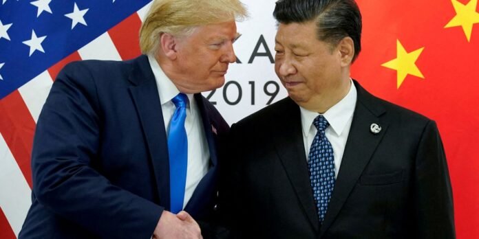 Two male world leaders shake hands in front of US and China flags behind them.