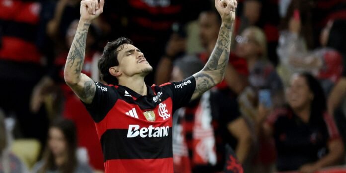 Soccer player in a red-and-black Flamengo jersey with arms raised in celebration on the field.