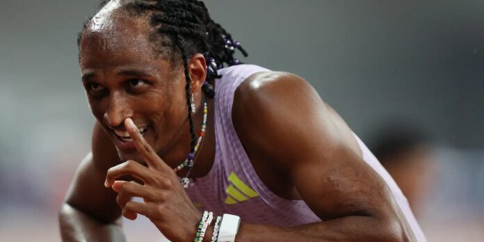Athlete in a lavender singlet smiles while placing a finger to lips in a shushing gesture.