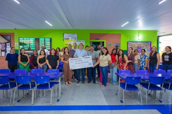 Group of adults posing and holding a large ceremonial check in a bright green-walled classroom with blue chairs.