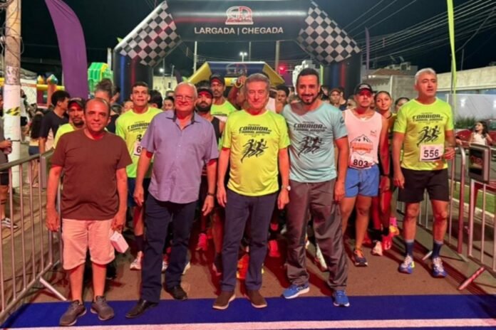 Group of runners at a night race start under a checkered arch that reads LARGADA CHEGADA, posing for a photo behind barriers.