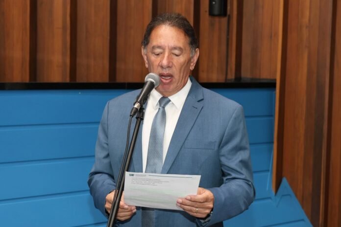 Man in a blue suit speaks into a microphone while reading from a sheet of paper in hand.
