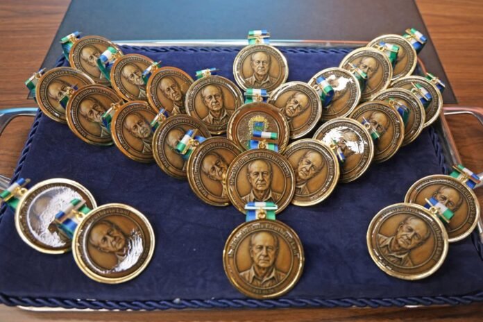 Collection of bronze medallions bearing a man's portrait, laid out on a blue velvet tray with small ribbons attached to each medal.