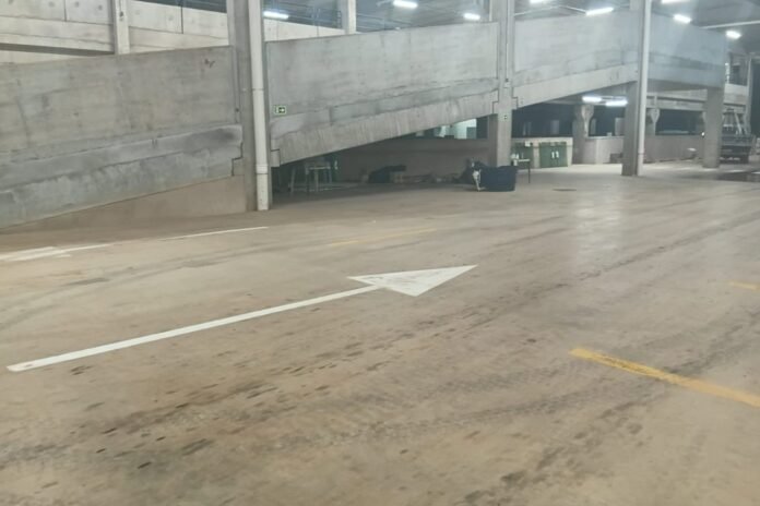 Indoor parking garage with a white directional arrow painted on the concrete floor, pointing left, under a concrete ramp and pillars.