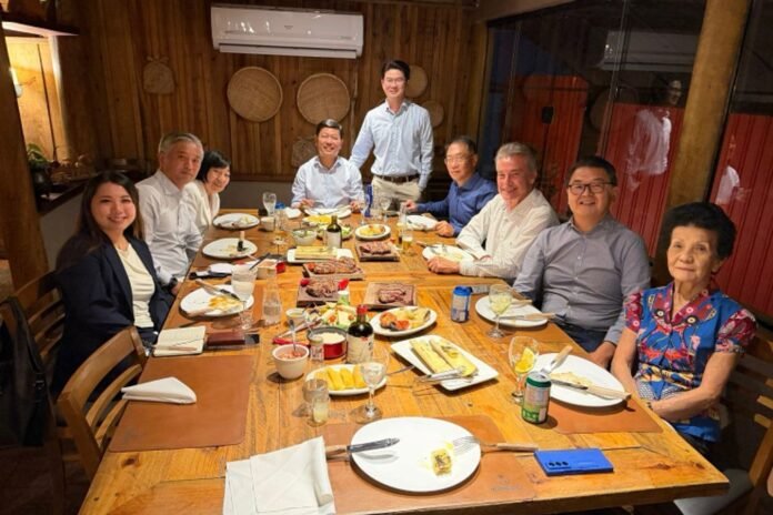 Twelve people dining around a long wooden table in a restaurant, with plates and drinks.