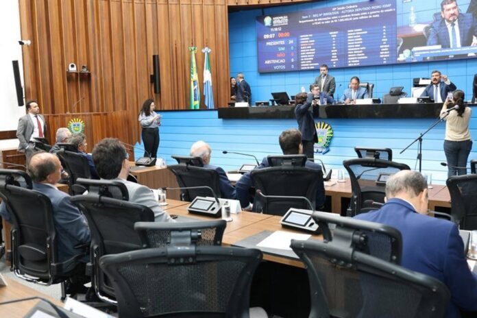 Parliamentary chamber with officials seated at desks on a blue dais and visitors in the foreground during a session.
