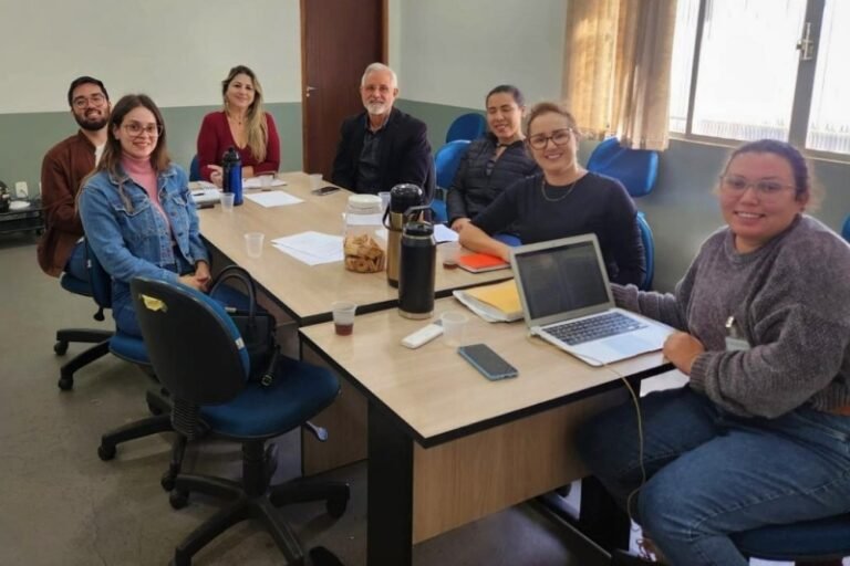 Eight people sit around a wooden conference table in a bright meeting room, smiling at the camera.
