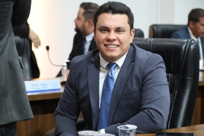 Smiling man in a navy suit and blue tie seated at a conference table in a meeting room