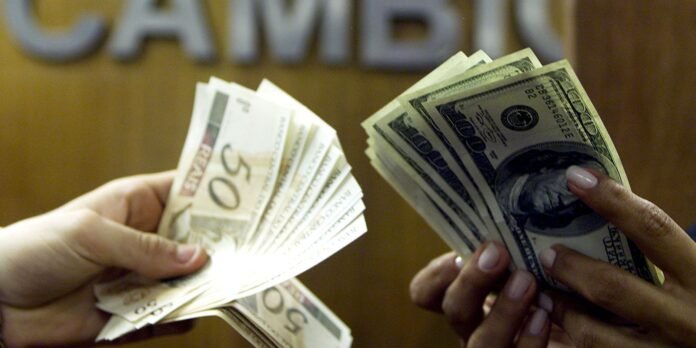 Two hands exchanging money: fan of euro banknotes on the left and a fan of US $100 bills on the right, in focus against a blurred background.