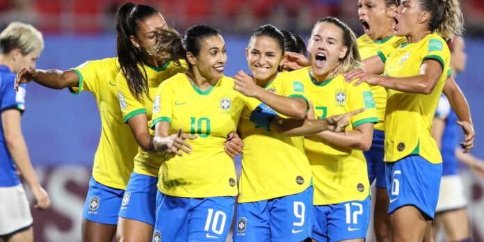 Brazilian women’s soccer players in yellow jerseys celebrate together on the field during a match.