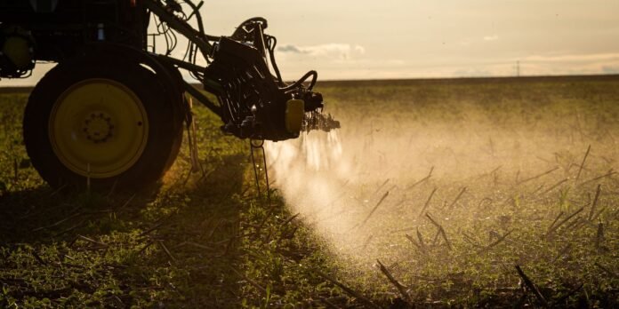 Farm spray rig attached to a tractor releasing a mist over a harvested field at sunset, irrigating crops.