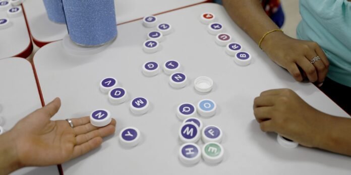 Children's hands arranging purple-letter circular tokens on a white table during a spelling activity.
