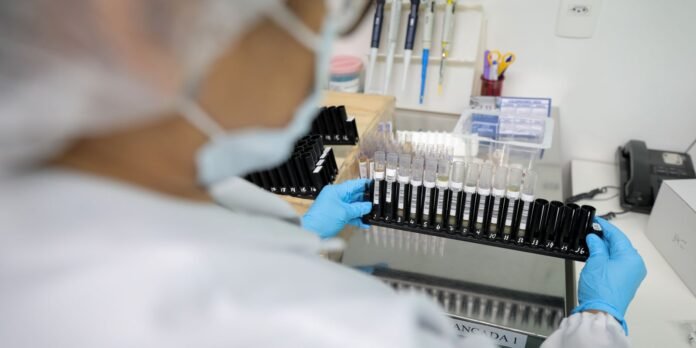 Lab technician wearing a mask and blue gloves arranges a rack of numbered test tubes in a laboratory workbench.