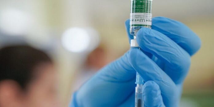 Gloved hand drawing liquid from a vial into a syringe for vaccination, close-up.