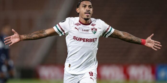 Soccer player in white kit with arms wide, celebrating on the pitch, sponsor 'SUPERBET' visible on jersey.