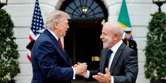 Two men in suits shake hands in front of a government building, with US and Brazilian flags visible in the background.
