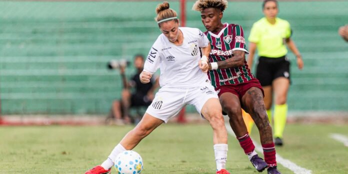 Two female soccer players chase the ball during a match: one in white, one in striped maroon-green, with a neon-clad referee in the background.