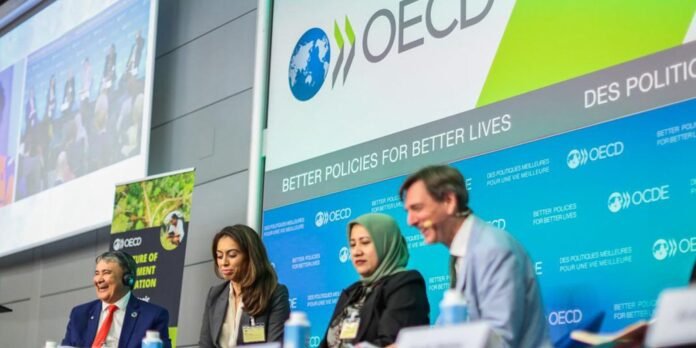 Panel of four speakers on a stage at an OECD conference, backdrop reads 'Better Policies for Better Lives'.