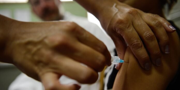 Healthcare worker administers a vaccine injection into a patient’s upper arm; hands and syringe in focus.