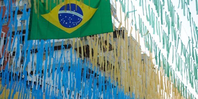 Brazilian flag hanging among blue, yellow, and green paper streamers decorating a street festival.